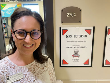 Rebecka Peterson stands in front of her classroom sign that has a USD logo on it.