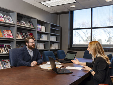 Travis Loof and Rachel Spinks work together across a table, talking with their hands.