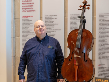 Ken Cancelosi stands next to a cello.