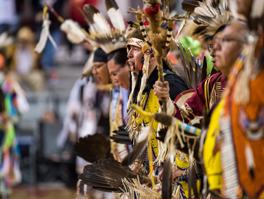 Dancers in regalia stand next to each other and bow their heads.