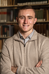 Caleb Swanson in front of a bookcase with his arms crossed.