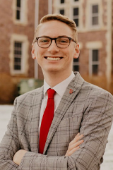 Caleb Weiland stands with his arms crossed in front of a building on USD's campus.